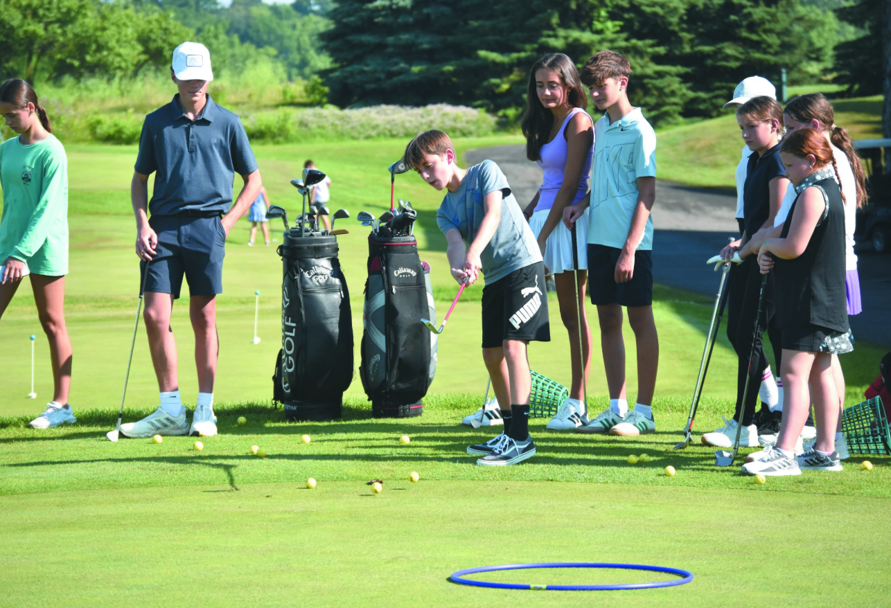 Student volunteer teaching a group of Baltimore youth how to grip a golf club on a practice green